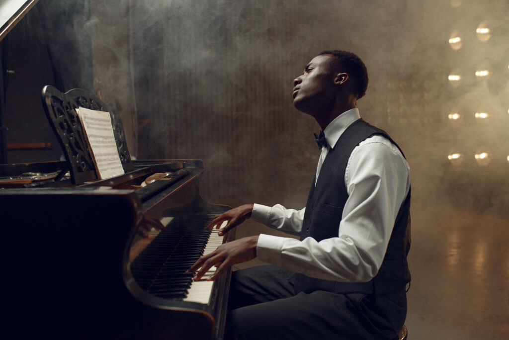 Ebony grand piano player playing on the stage with spotlights on background.