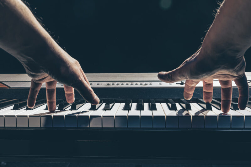 Male hands play the keys of the piano in the dark close-up, the concept of musical creativity.